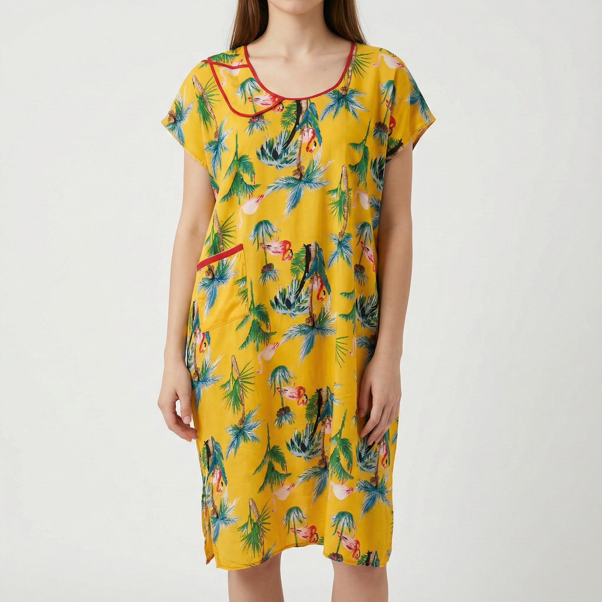 Manta Wayuu corta de color amarillo con estampado de palmeras y flamencos, cuello redondo con ribete rojo y bolsillo lateral.