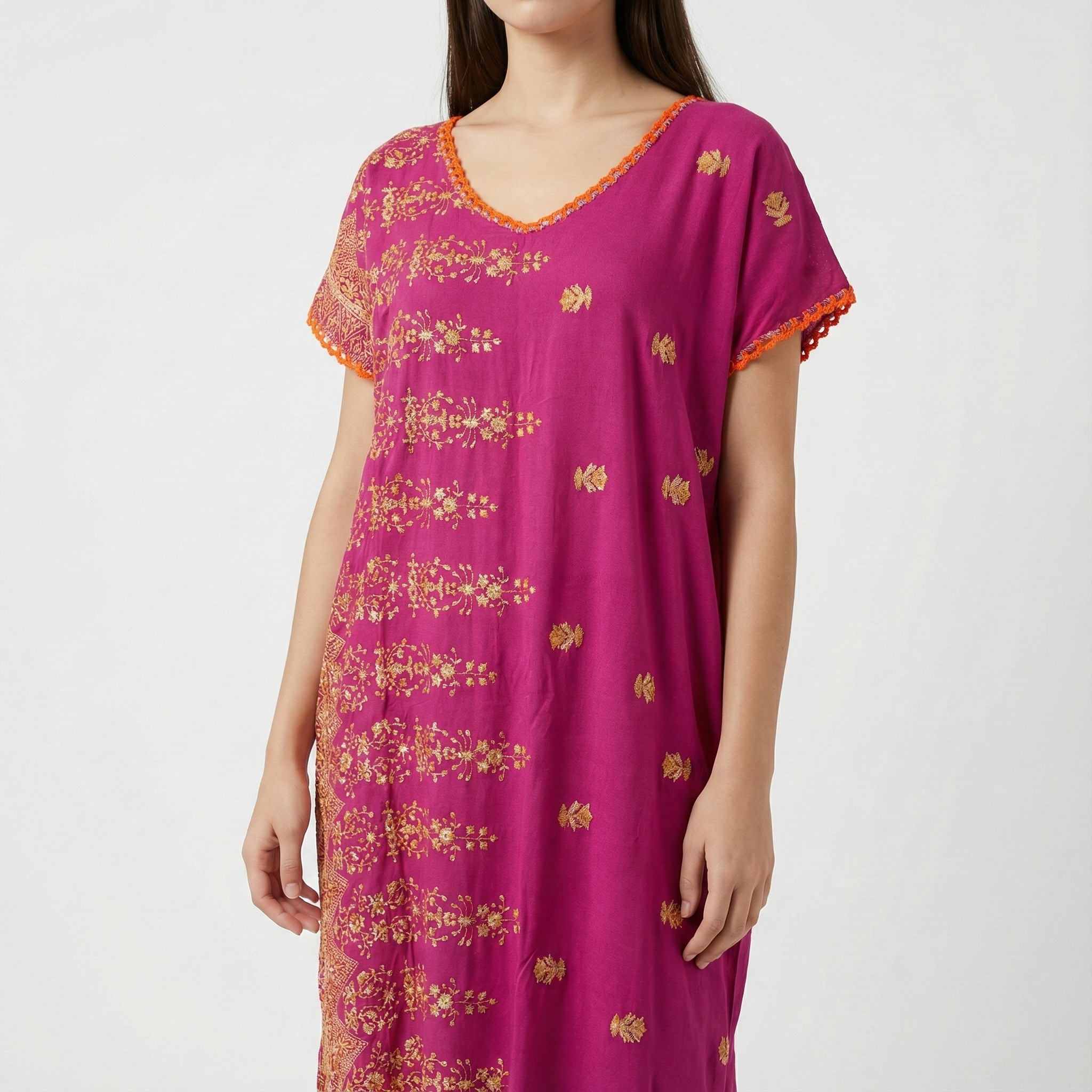 Manta Wayuu corta color magenta con bordados florales dorados y detalles de ganchillo naranja en el cuello y las mangas.