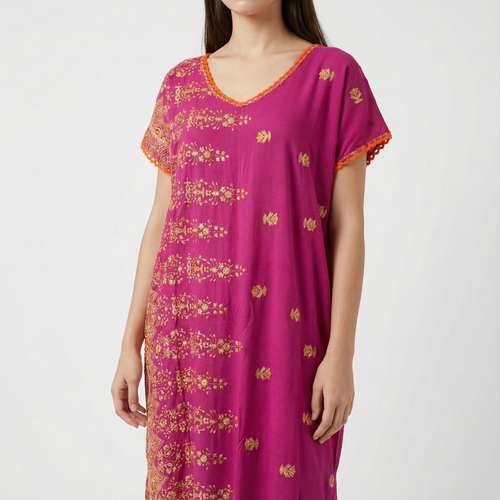 Manta Wayuu corta color magenta con bordados florales dorados y detalles de ganchillo naranja en el cuello y las mangas.