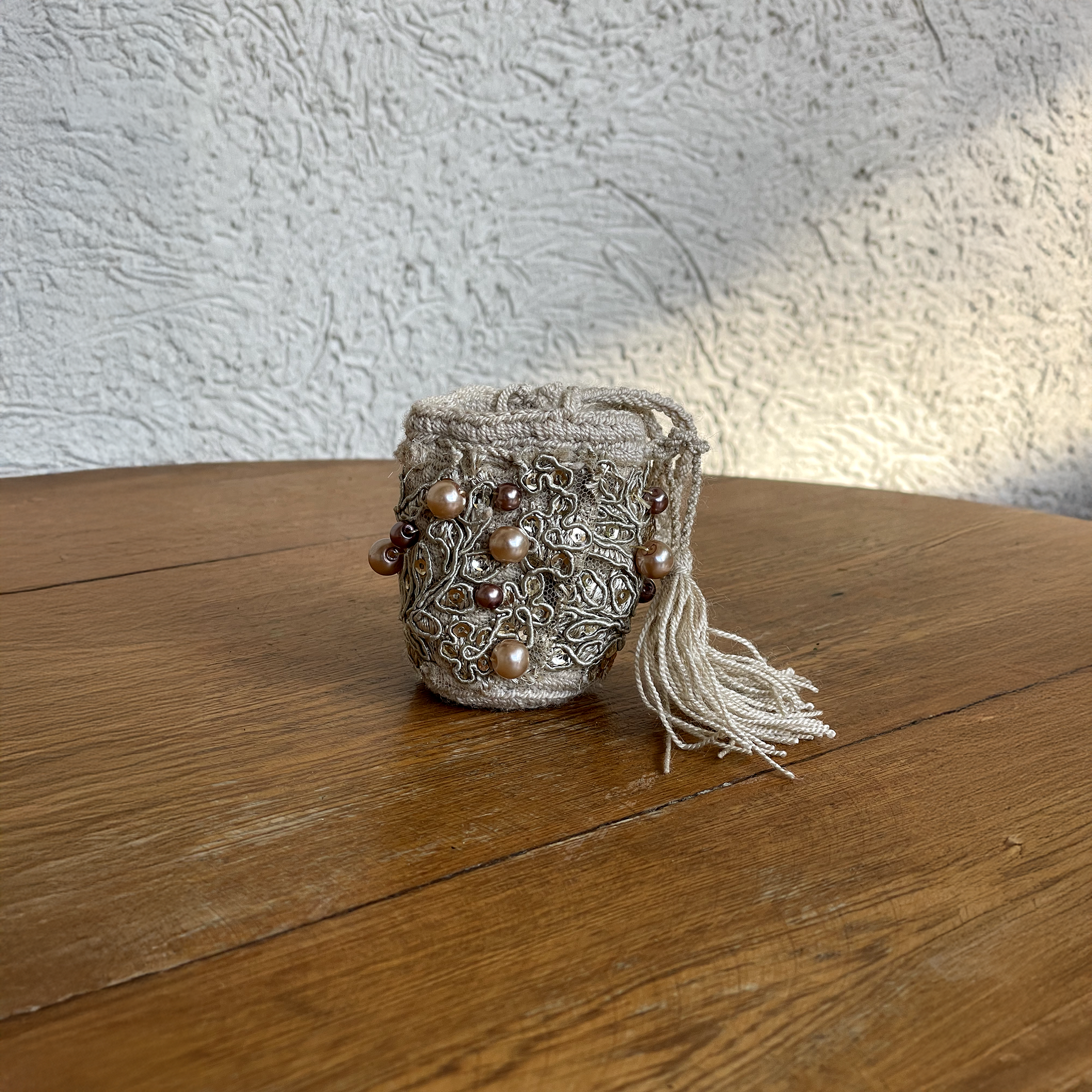 Mini mochila Wayúu beige con bordados metalizados plateados, perlas en tonos tierra y borla de hilos crema.