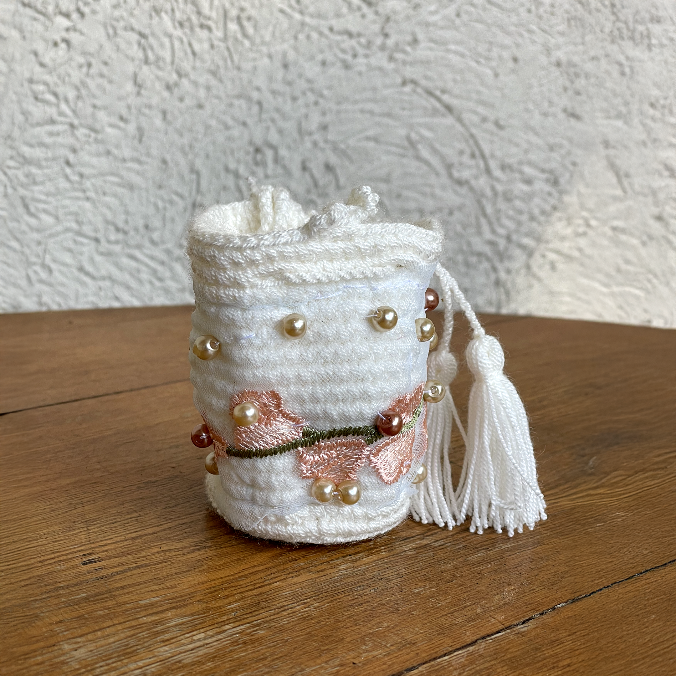 Mini mochila Wayúu blanca con bordado de flores rosadas, perlas y borlas blancas sobre madera
