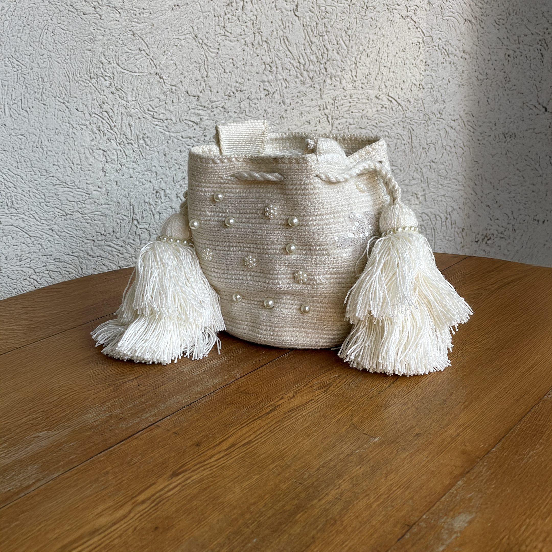 Mochila Wayúu artesanal blanca con bordado de perlas y lentejuelas, terminada con borlas dobles voluminosas.