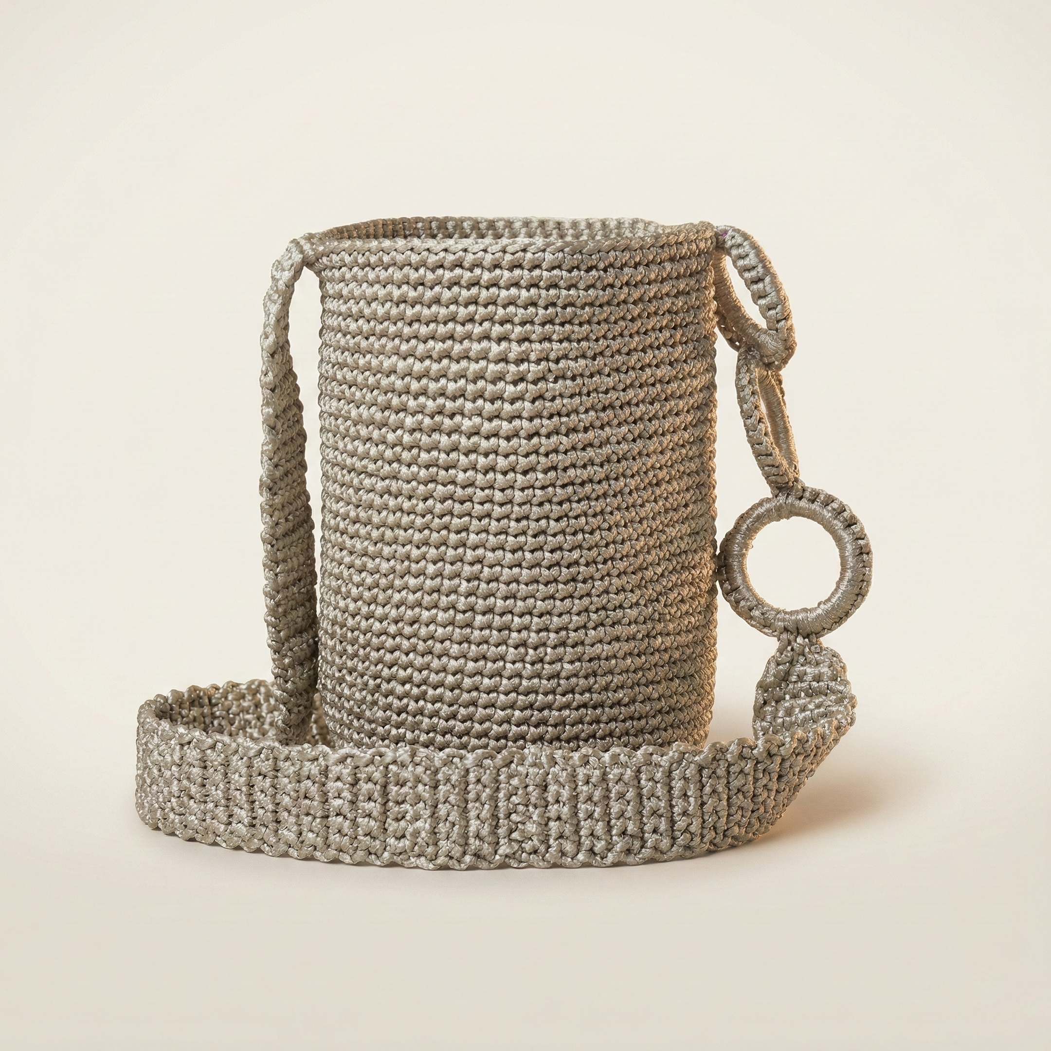Mochila Wayúu cilíndrica pequeña en color gris plata unicolor, con tejido denso y una gasa ancha conectada por anillas forradas del mismo tono.
