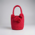 Mochila Wayúu de mano en color rojo vibrante con asa trenzada corta y cuatro pompones decorativos grandes en el mismo tono.