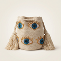 Mochila artesanal color arena con bordados de ojos en cristales azules y dorados, acabados de lujo y borlas grandes.