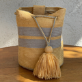Mochila Wayuu tejida a mano con diseño de rayas horizontales en color amarillo y gris, incluye cierre de cordón trenzado y borla decorativa amarilla.